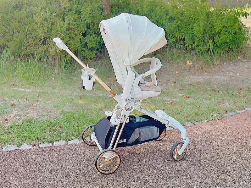 잔디와 산책로 옆에 세워 둔 흰색 덮개의 에이블 코지샤인 유모차