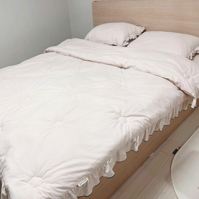 침대 위에 펼쳐 둔 베이지색 차렵이불과 베개