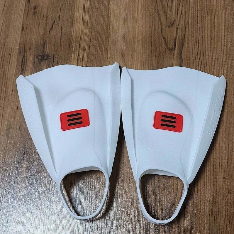 나무 바닥 위에 나란히 놓인 흰색 숏핀 한 쌍, 중앙에 빨간 패치와 세 줄 로고