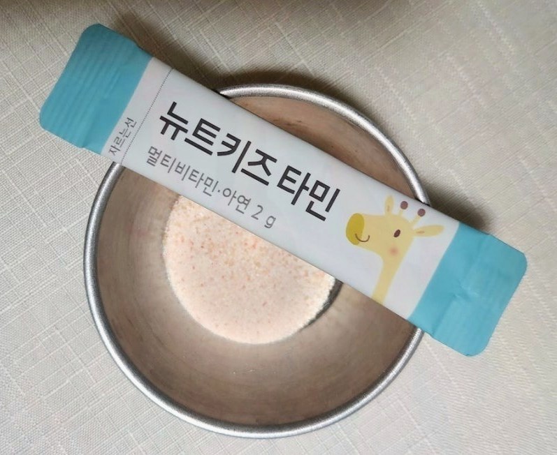 뉴트키즈 타민 스틱 한 포가 가루가 담긴 금속 그릇 위에 놓인 모습