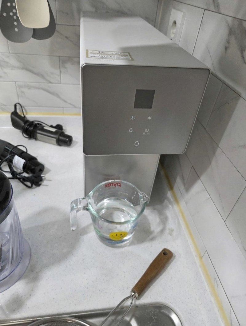 싱크대 상판 위에 올려 둔 슬림한 정수기와 계량컵