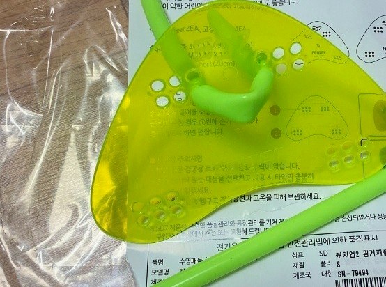 비닐 포장 위에 놓인 형광 노랑 핑거패들 한 쌍과 연두색 끈