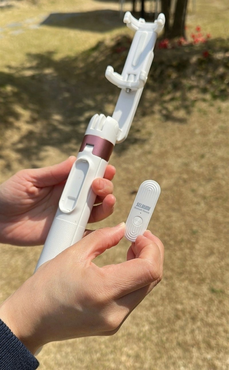 봉을 길게 뽑아 휴대폰을 꽂은 셀카봉과 리모컨을 든 손