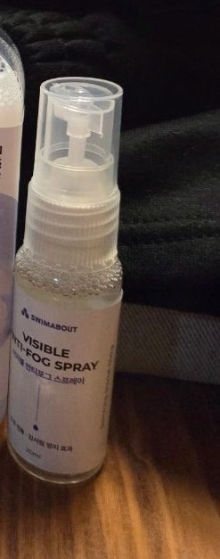 SWIMABOUT 로고와 VISIBLE ANTI-FOG SPRAY가 적힌 투명 스프레이 병이 수영 가방 옆에 있는 모습